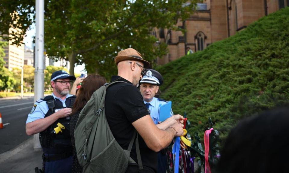 Police on Thursday morning speak to a man removing ribbons placed along a fence by supporters of sexual abuse survivors outside St Mary’s Cathedral where ribbons were removed overnight.