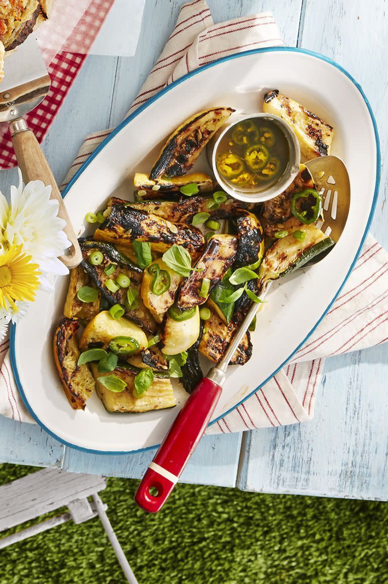 grilled summer squash on an oval serving plate with a small bowl of lemon scallion dressing