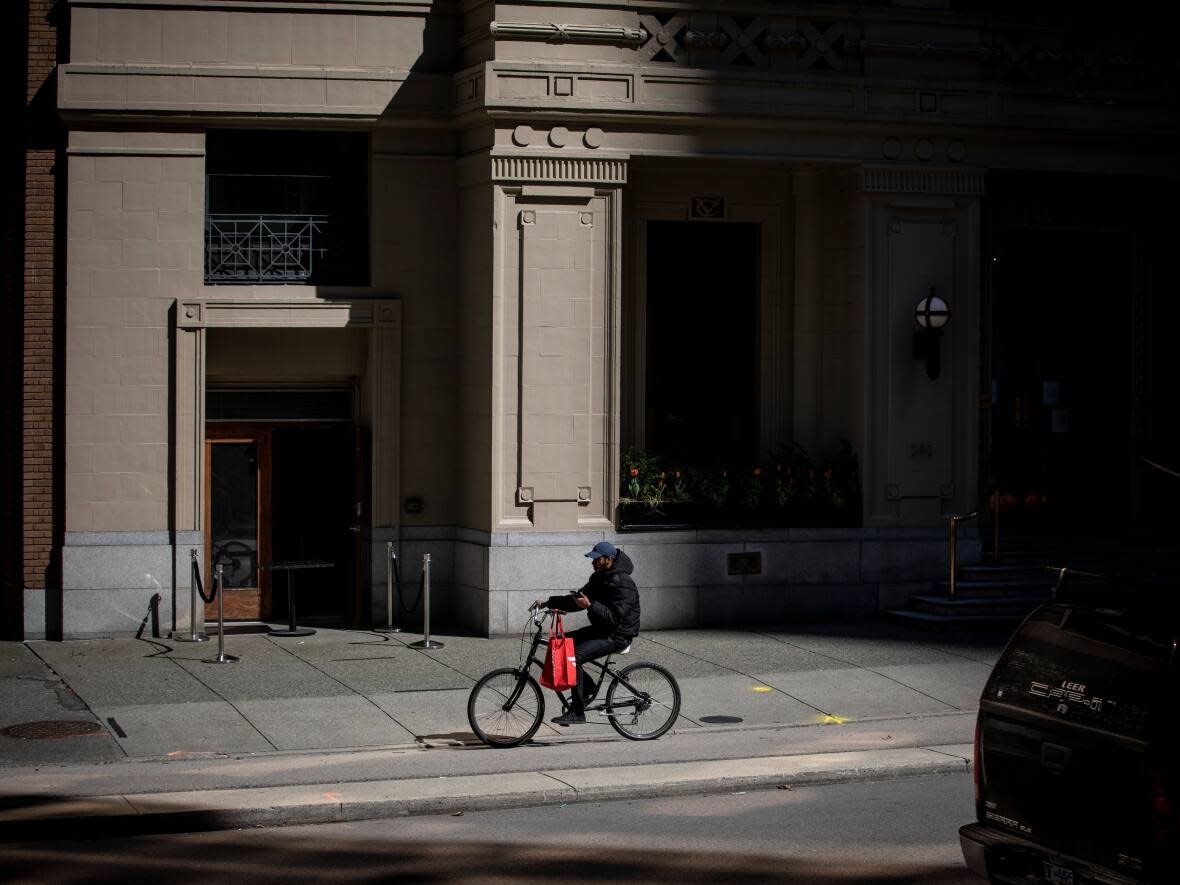 A DoorDash food delivery worker rides his bicycle through downtown Vancouver. The B.C. government has passed legislation permanently capping the fees that delivery apps can charge restaurants. (Ben Nelms/CBC - image credit)
