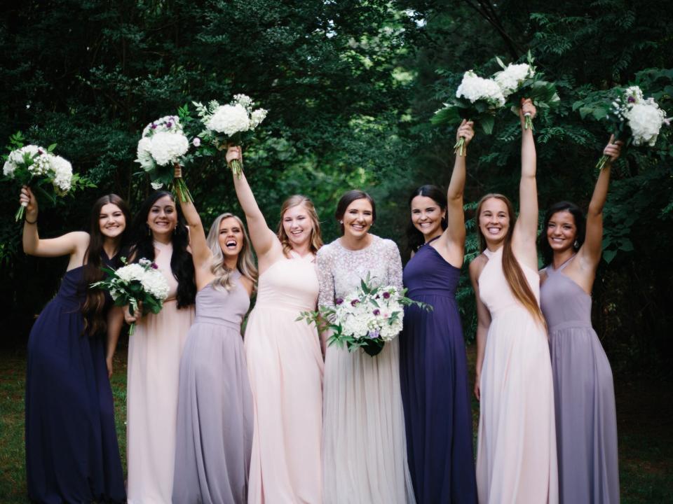 A bride stands in the center of her bridesmaids, who raise their bouquets in their hands.