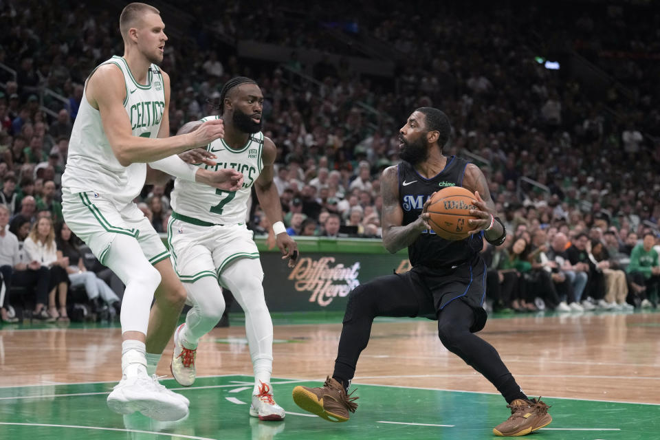 Dallas Mavericks guard Kyrie Irving, right, drives toward the basket as Boston Celtics center Kristaps Porzingis, left, and guard Jaylen Brown, center, defend during the second half of Game 1 of the NBA Basketball Finals, Thursday, June 6, 2024, in Boston. (AP Photo/Charles Krupa)