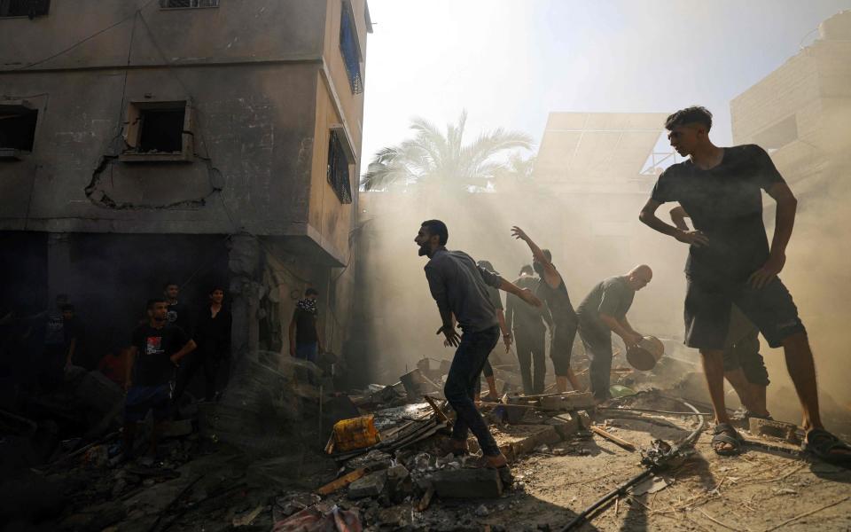 Palestinians react as they check the rubble of a building, in Khan Yunis