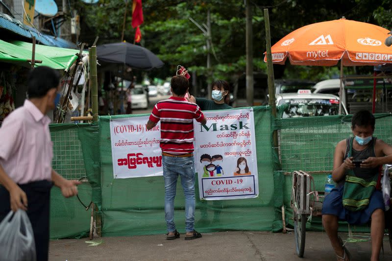 A woman passes a package to a man behind a makeshift barricade, blocking off a street to prevent the spread of the coronavirus disease in Yangon