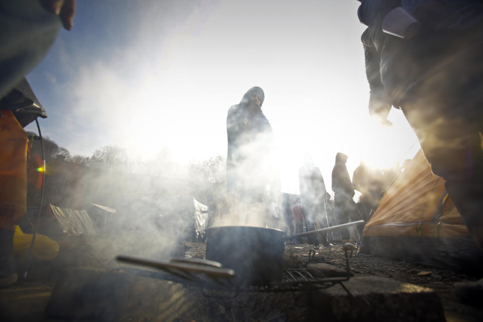 In this Sunday, Nov. 18, 2019 photo migrants cook outdoors while others wait for food distribution at a camp in Velika Kladusa, Bosnia, close to the border to Croatia. The approach of the tough Balkan winter spells tough times for the migrants that remain stuck in the region while trying to reach Western Europe, with hundreds of them staying in make-shift camps with no heating or facilities.(AP Photo/Amel Emric)