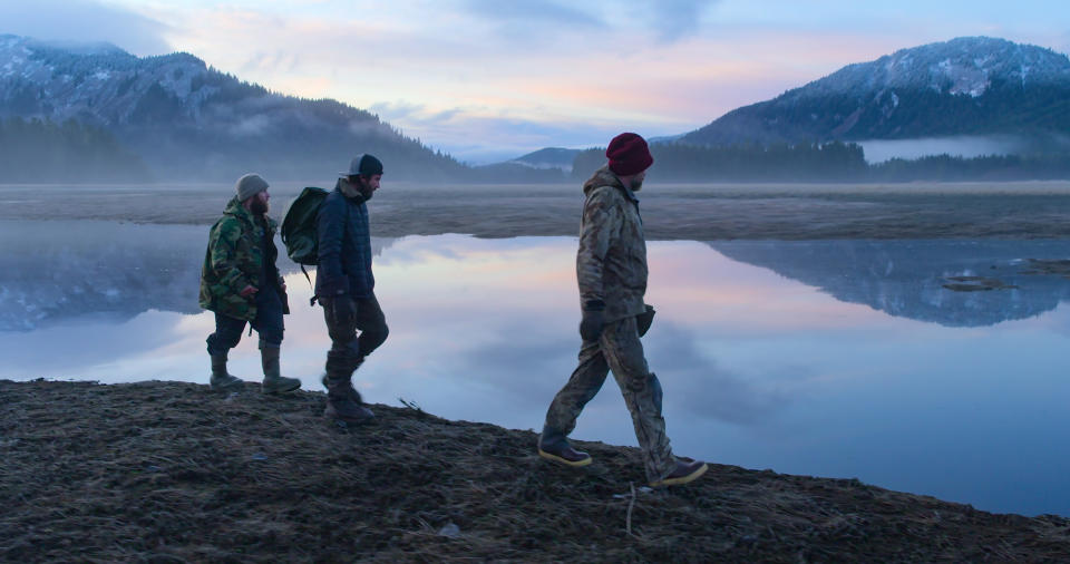 three people dressed warmly walking along a water's edge