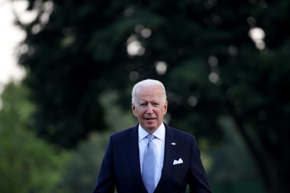 US President Joe Biden waring a blue suit in front of a lush green background of trees.