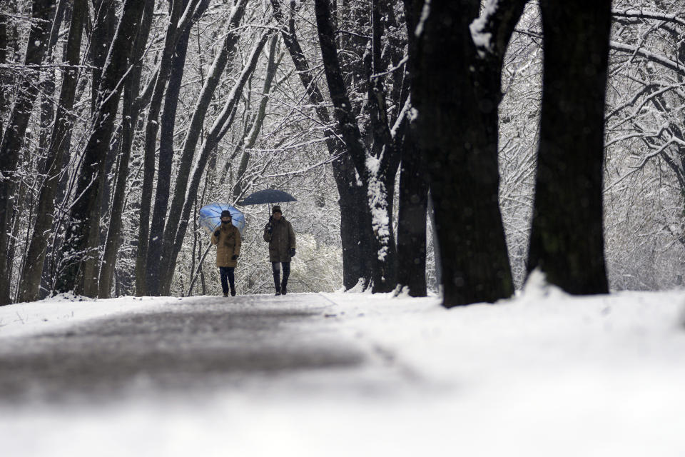People walk through a snow covered park in Belgrade, Serbia, Sunday, Feb. 26, 2023. Serbia and the rest of the region were hit by a sudden weather change this weekend that brought rain and snow after a warm period. (AP Photo/Darko Vojinovic)