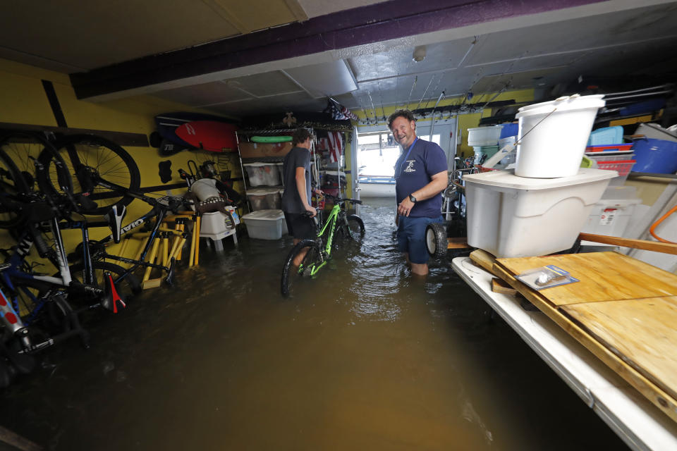 Rudy Horvath Jr., left, moves his bicycle from his home, a boat house in the West End section of New Orleans, as his father, Rudy Horvath Sr., right, looks on after it took on water from a rising storm surge from Lake Pontchartrain in advance of Tropical Storm Cristobal, Sunday, June 7, 2020. (AP Photo/Gerald Herbert)