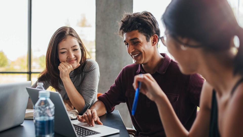 Indoor shot of three young students studying together using laptop.