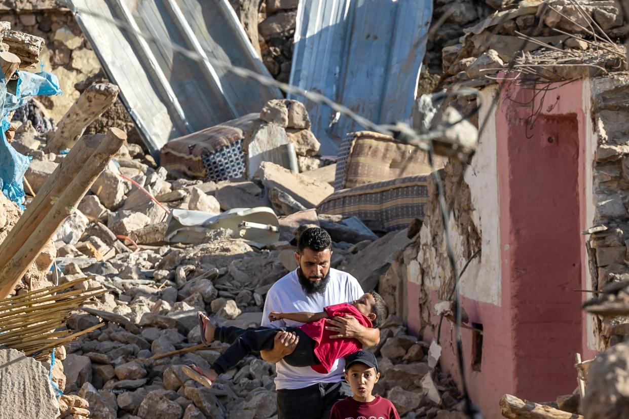 A man carries a boy as he walks past destroyed houses after an earthquake in the mountain village of Tafeghaghte, southwest of Marrakech (AFP vis Getty Images)