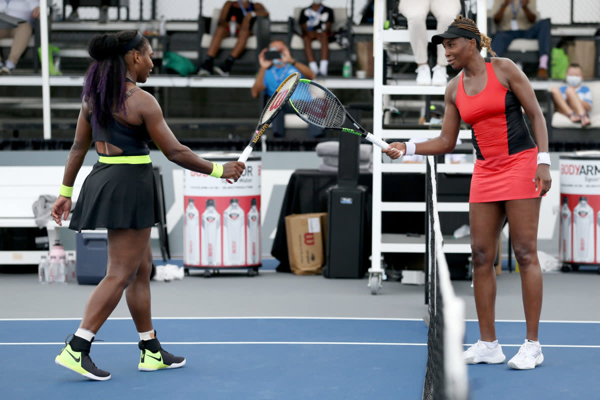 Serena Williams and her sister Venus touch rackets.