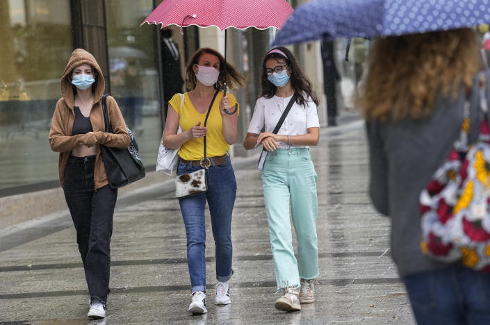 People wearing a face masks to protect against coronavirus walk along the Champs Elysees avenue in Paris, Monday, July 12, 2021. France's President Emmanuel Macron is hosting a top-level virus security meeting Monday morning and then giving a televised speech Monday evening, the kind of solemn speech he's given at each turning point in France's virus epidemic. (AP Photo/Michel Euler)