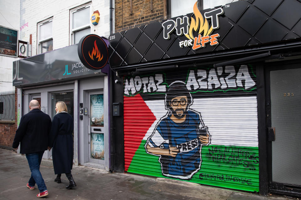 Members of the public pass artwork featuring an image of Palestinian journalist Motaz Azaiza on a Palestinian flag painted on a shop blind in Tower Hamlets on 21st January 2024 in London, United Kingdom. There are many visible symbols of solidarity with Palestinians in the Tower Hamlets area of London, including pro-Palestinian street art produced by Paint for Palestine and Palestinian flags. (photo by Mark Kerrison/In Pictures via Getty Images)