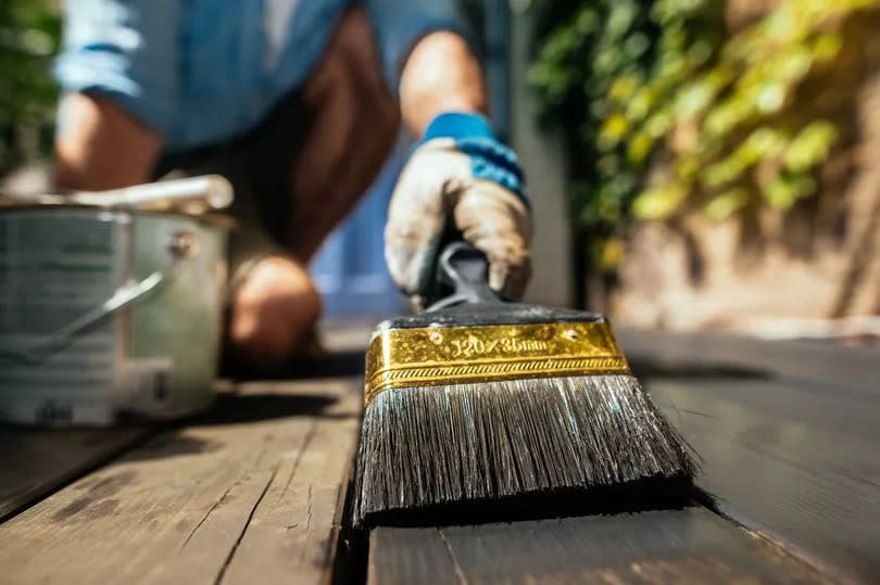 Man preparing wooden deck with brush and  organic oil at home,close-up.