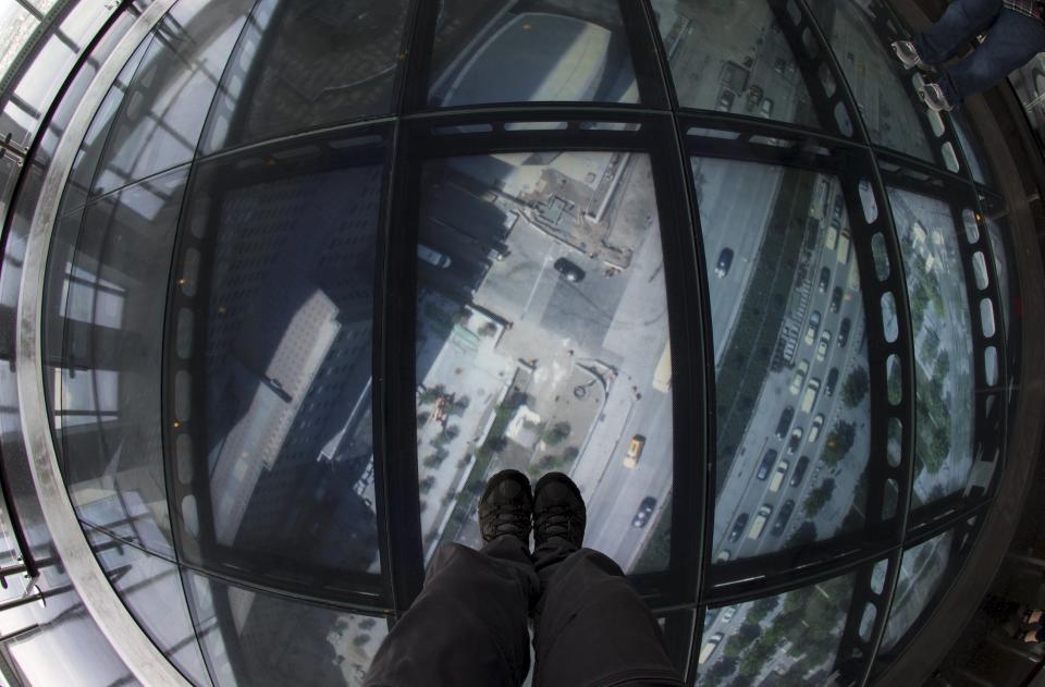 A member of the media stands on the SkyPortal, a 14-foot wide disc that delivers high-definition live video footage from the street below, in the One World Observatory observation deck on the 100th floor of the One World Trade center tower in New York during a media tour of the site May 20, 2015. One World Observatory will open to the public on May 29. (REUTERS/Mike Segar)