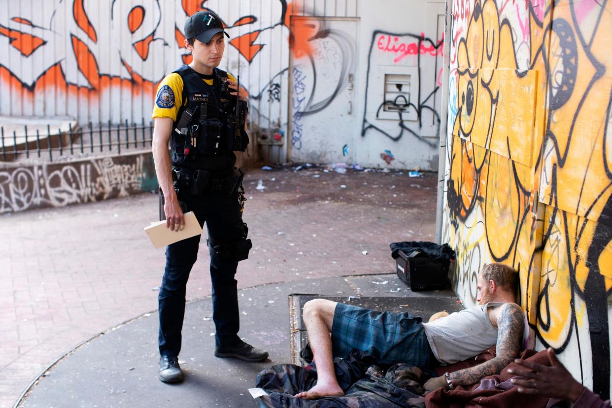 Officer Donny Mathew of the Portland Police Bureau's bike squad, stands next to a person who appears to be passed out on Thursday, May 18, 2023, in downtown Portland, Ore. Three years ago, nearly two-thirds of Oregon voters approved a ballot measure decriminalizing illicit drugs, backing the idea that addiction treatment is more effective than jail. But now, public drug use in cities such as Portland and a surge in fentanyl overdose deaths have created a backlash against the first-in-the-nation law. (Beth Nakamura/The Oregonian via AP)