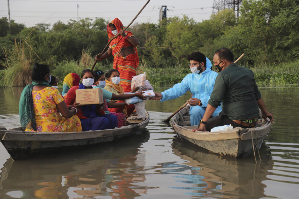 Indian man Himanshu, wearing personal protective suit as a precaution against the coronavirus distributes free aid procured by him to people living in a small island in River Yamuna in New Delhi, India, Wednesday, June 2, 2021. (AP Photo/Amit Sharma)