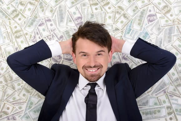 A smiling businessman lying on a bed of cash.