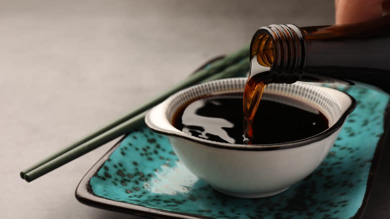 Person pouring soy sauce into small bowl