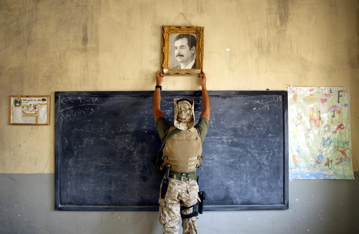 A U.S. Marine reaches above a blackboard to take down a picture of Saddam Hussein.