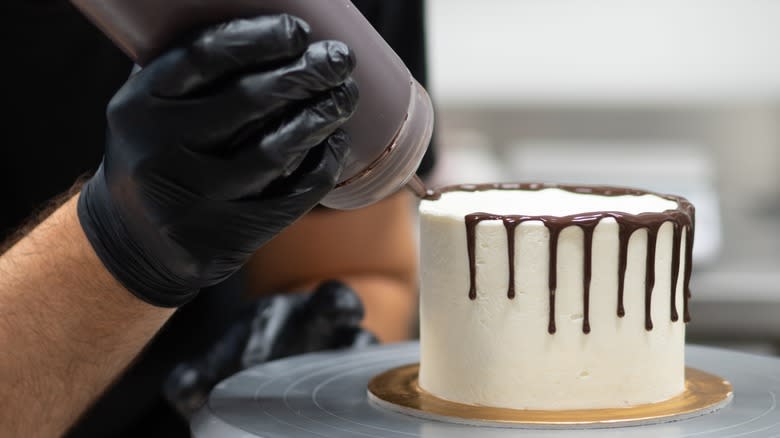person using squeeze bottle to create ganache drips on cake