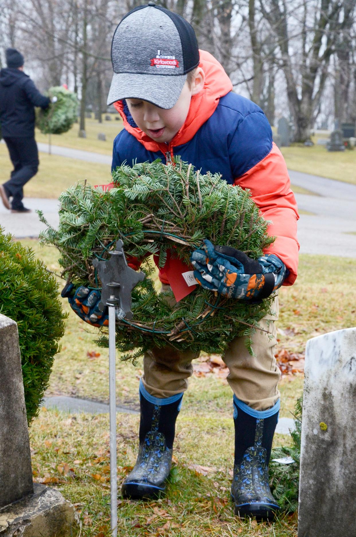 Owen Byron, 7, of Petoskey places a wreath at a veteran's grave on Saturday, Dec. 16, 2023 at Greenwood Cemetery during the annual Wreaths Across America event.