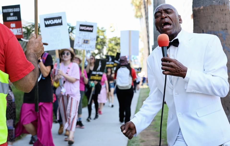 LOS ANGELES, CALIFORNIA - JULY 28: Lenny Hoops sings on the picket line as striking SAG-AFTRA and Writers Guild of America (WGA) members pass outside Netflix studios on July 28, 2023 in Los Angeles, California. Starbucks workers also joined the picket line in a show of support as part of a Starbucks Workers United ‘The Union is Calling’ summer bus tour across 13 cities in an effort to unionize more Starbucks stores with workers calling for a living wage and other protections amid a so-called ‘hot labor summer’. (Photo by Mario Tama/Getty Images) ORG XMIT: 776012561 ORIG FILE ID: 1577142041