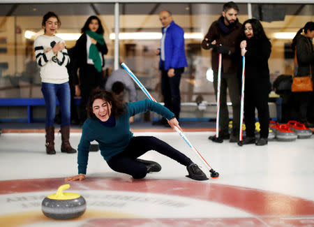 A Yazidi refugee from Kurdistan falls over after throwing a rock as she learns the sport of curling at the Royal Canadian Curling Club during an event put on by the "Together Project", in Toronto, March 15, 2017. REUTERS/Mark Blinch