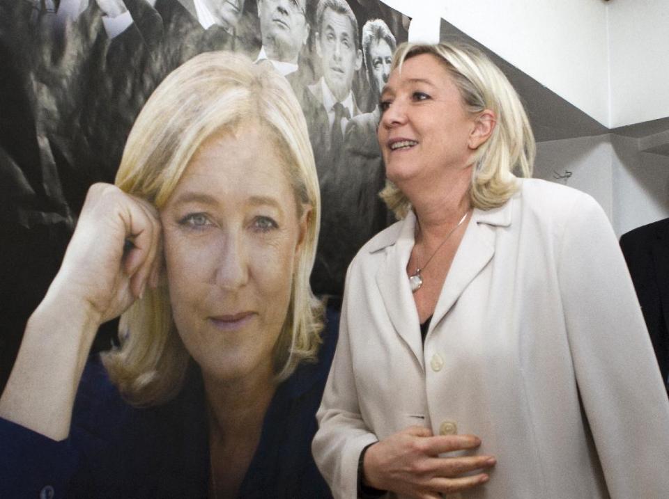 FILE - - In this March 8, 2014 file photo, French far-right party leader Marine Le Pen walks past a poster of her at the party headquarters in Henin-Beaumont, northern France, as part of the municipal campaign. Marine Le Pen sees political gold in the abandoned coal mines of northern France that once pumped life, jobs and an identity into places like Henin-Beaumont, a bleak town that the far-right leader says is the avant-garde of her anti-immigration party's march to power. (AP Photo/Jacques Brinon, File)