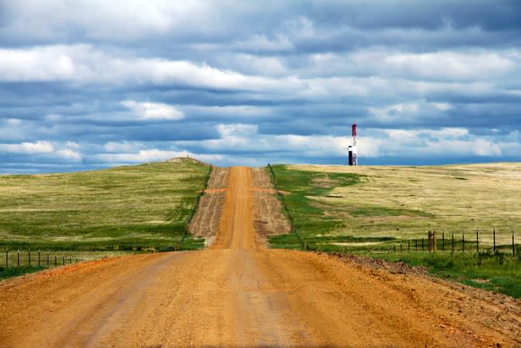 A dirt road leading up to a drilling rig that's over the hill.