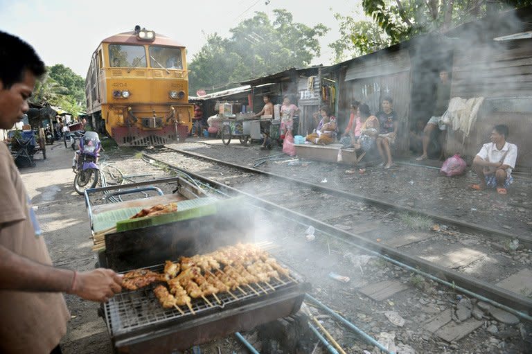 A man cooks barbecue chicken as a train passes by shack houses in Bangkok. Thailand's cabinet has approved a plan to spend $68 bn on a high-speed railway and other transportation mega projects to drive the nation's economic development