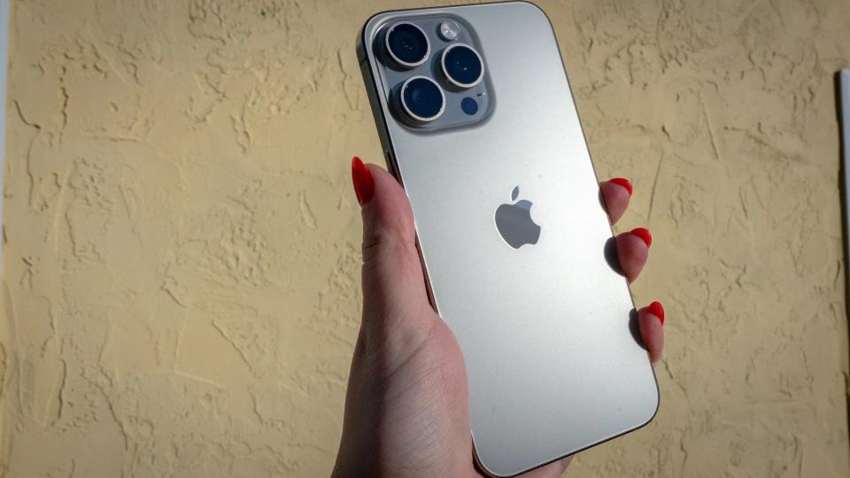 The iPhone 15 PRo with the backplate showing the apple logo in front of a stucco wall.