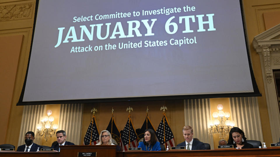 Rep. Liz Cheney and fellow committee members sit at a bench below a screen reading: Select Committee to Investigate the January 6th attack on the United States Capitol.