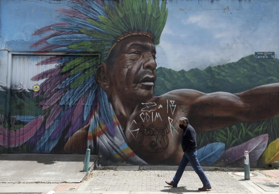 A man wearing a mask amid the spread of the new coronavirus walks past a mural in Bogota, Colombia, Friday, Oct. 16, 2020. (AP Photo/Fernando Vergara)