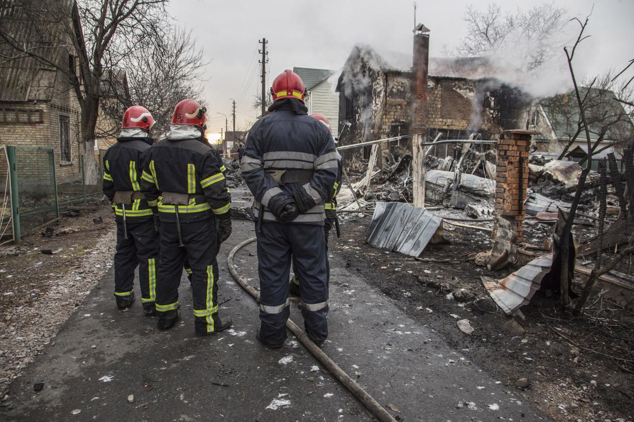 Ukrainian firefighters look at fragments of a downed aircraft seen in in Kyiv, Ukraine, Friday, Feb. 25, 2022. It was unclear whose aircraft crashed and who brought it down amid the Russian invasion in Ukraine. Russia is pressing its invasion of Ukraine to the outskirts of the capital after unleashing airstrikes on cities and military bases and sending in troops and tanks from three sides.