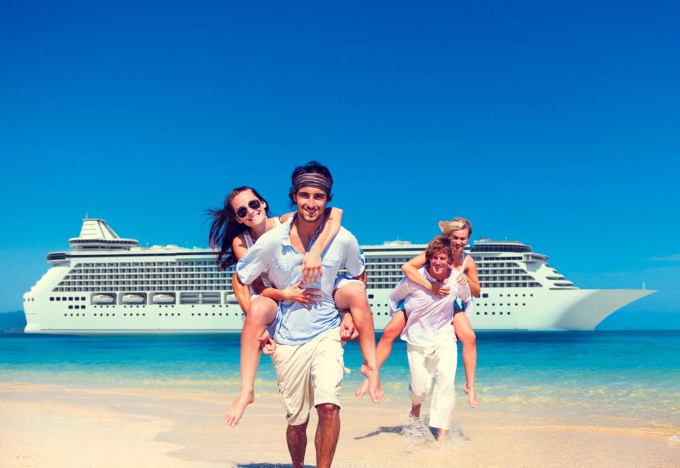 A group of travelers frolic on a beach with a cruise ship in the background.