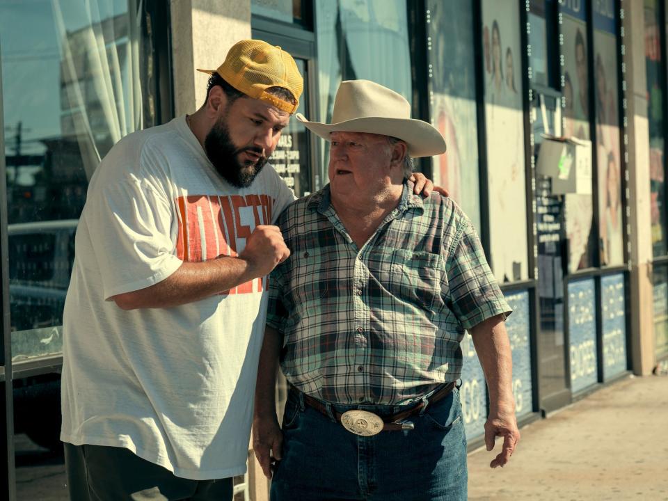 Two men standing outside a strip mall of storefronts.