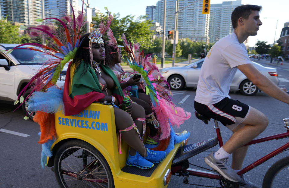 A rickshaw worker pedals costumed clients after they attended the Caribbean Carnival parade in Toronto, Canada, Saturday, July 30, 2022. The 55th annual parade returned to the streets after the COVID-19 pandemic cancelled it for two years in a row. (AP Photo/Kamran Jebreili)