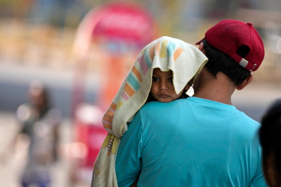 A man carries a child, head covered with a towel to protect from the heat, in Jammu, India (AP)