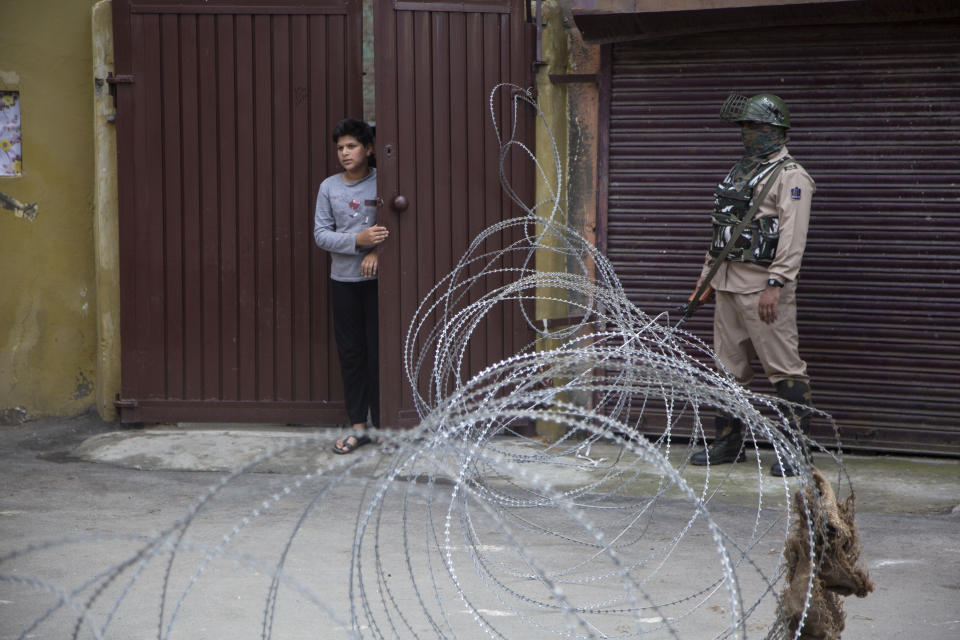 A young Kashmiri boy looks out from the gate of his house as an Indian paramilitary soldier stands guard at a check point during a restrictions in Srinagar, Indian controlled Kashmir, Saturday, Aug. 29, 2020. Authorities had imposed restrictions in parts of Srinagar, the region's main city, to prevent gatherings marking Muharram from developing into anti-India protests. (AP Photo/Mukhtar Khan)