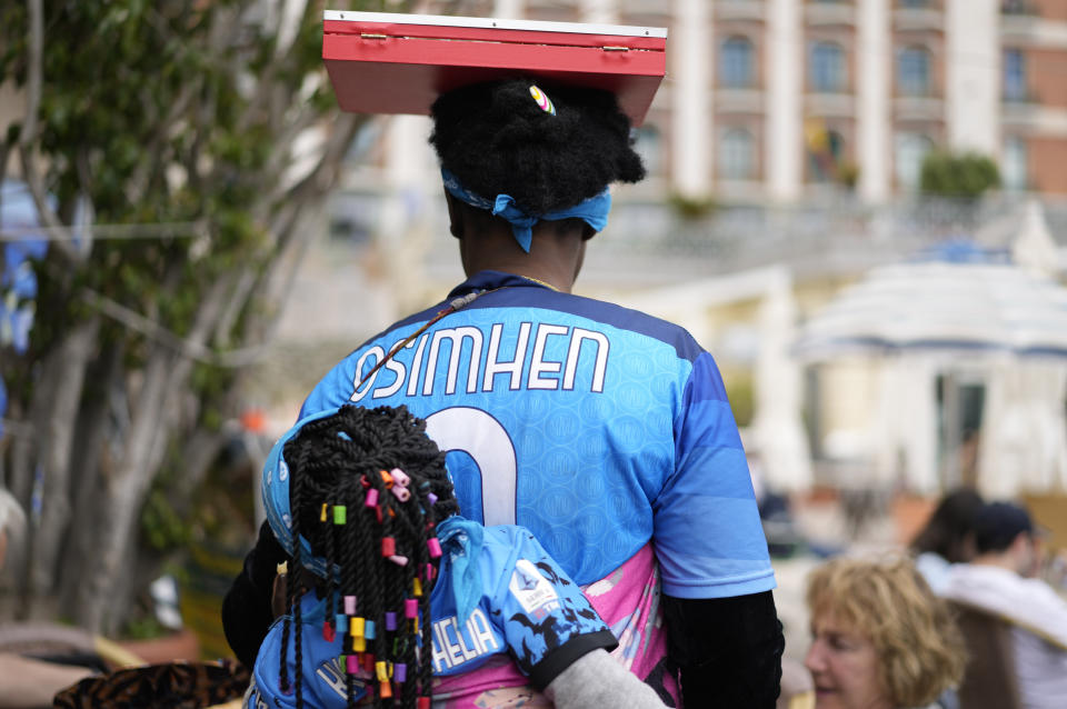 A woman street hawker walks wearing a Napoli soccer team striker Victor Osimhen jersey, in Naples, Italy, Thursday, May 4, 2023. (AP Photo/Andrew Medichini)