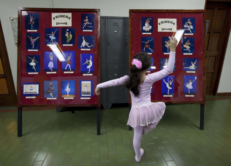 In this Aug. 28, 2012 photo, a young ballerina holds a pose as she looks at photos of ballet dancers at the National Superior Ballet School in Lima, Peru. Nearly 100 girls and boys from Colombia, Venezuela, Chile, France and Peru are submitting themselves to a week-long competition hoping to win medals from Peru's national ballet school _ and perhaps a grant to study in Miami. (AP Photo/Martin Mejia)