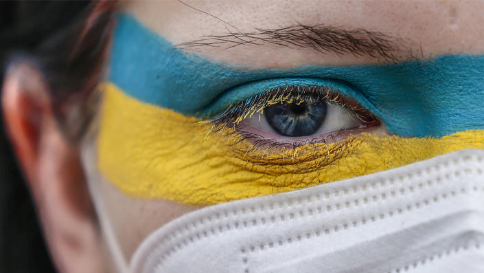 A young woman in a mask, her face painted the colors of the Ukrainian flag, at a protest.