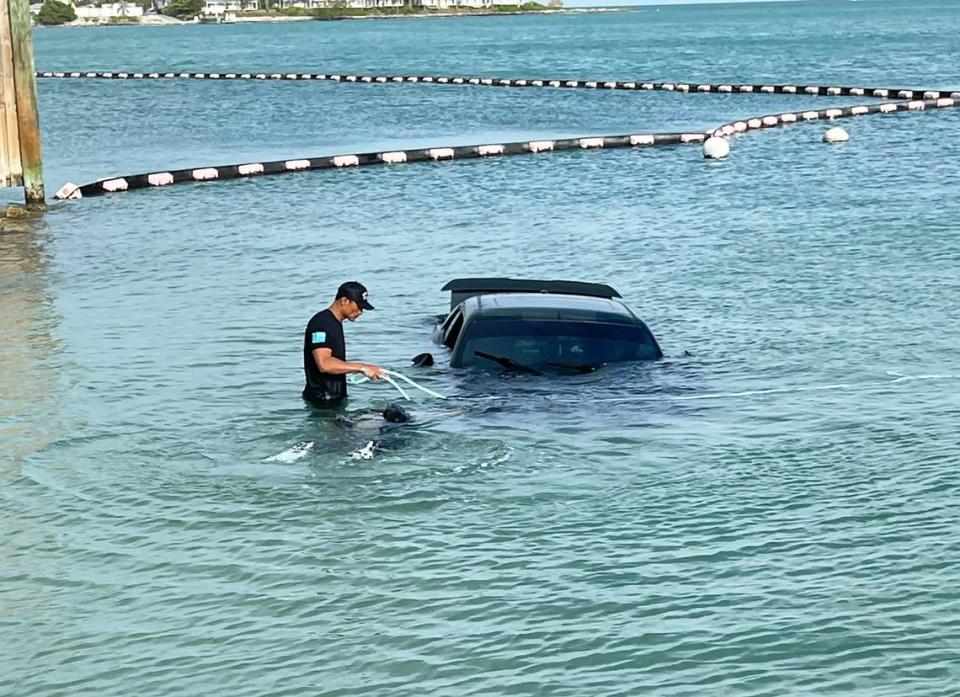 A Key West firefighter stands in the shallow water next to a sunken Dodge Challenger that police say a man drove into the ocean Sunday, April 28, 2024.