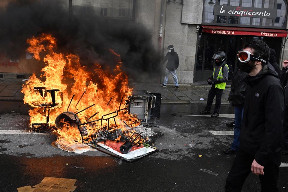 A demonstrator walks by burning debris during a rally against the law reforming the national pensions system, in Rennes, western France, March 23, 2023, a week after the government pushed a pensions reform bill through parliament without a vote. / Credit: DAMIEN MEYER/AFP/Getty