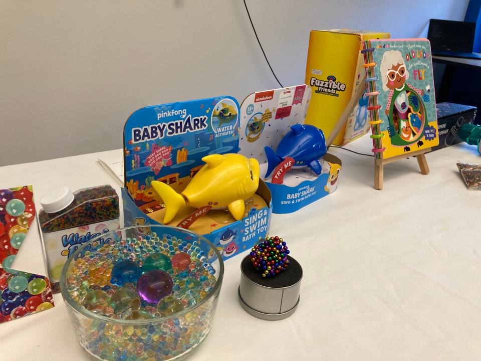Some of the troublesome toys on the list released by MassPIRG were displayed. The water beads pose multiple hazards from choking to illness, and the recalled Baby Shark toy, in yellow, had a sharp, rigid plastic fin that could cause lacerations. The board book has bindings that can be removed and pose a choking hazard.