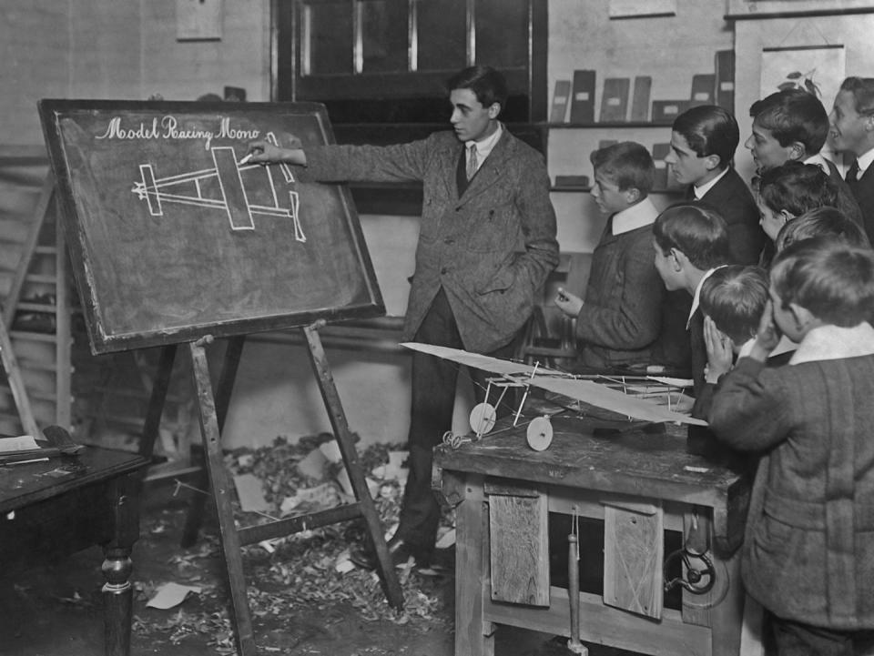 <p>A class of boys watch closely as their instructor teaches them how to create a model airplane. </p>