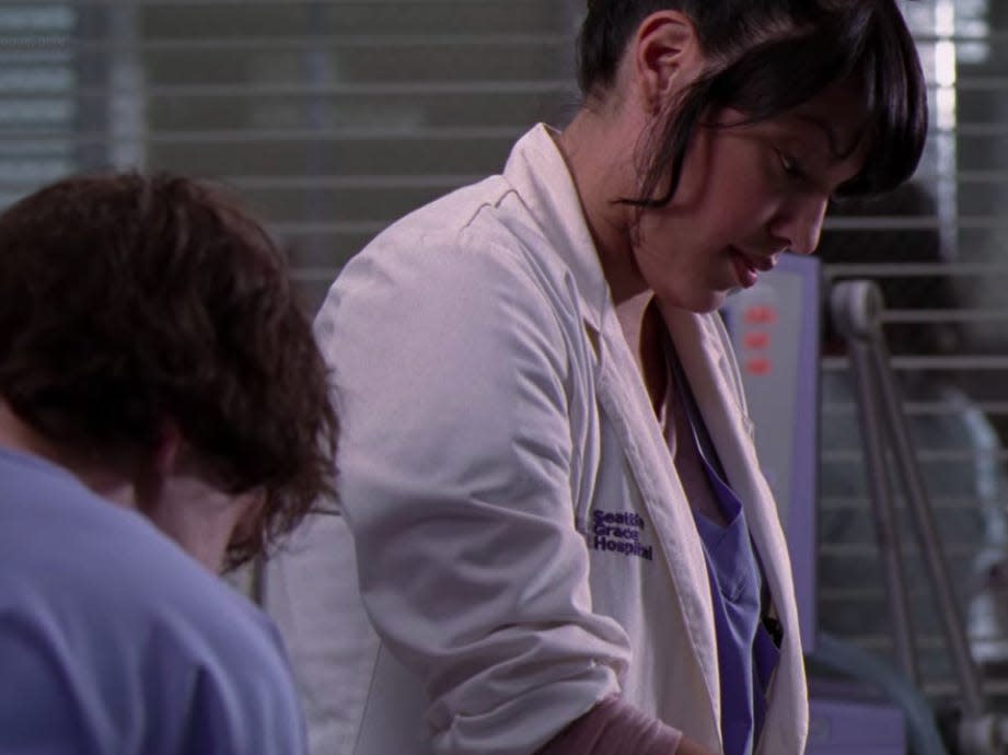 Sara Ramirez as Callie on Greys Anatomy in a hospital room and wearing scrubs and a coat