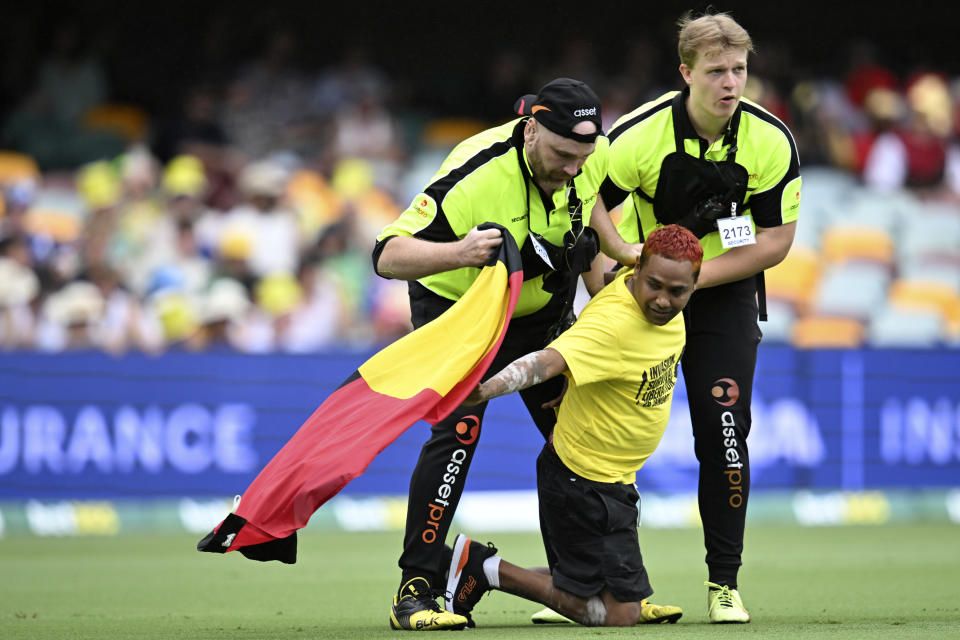 A protester, center, carrying an Aboriginal flag is apprehended by security on the second day of the cricket test match between Australia and the West Indies in Brisbane, Friday, Jan. 26, 2024. Thousands of Australians protested the anniversary of British colonization of their country with large crowds urging for Australia Day to be moved and for a day of mourning on the holiday some call "Invasion Day." (Darren England/AAP Image via AP)