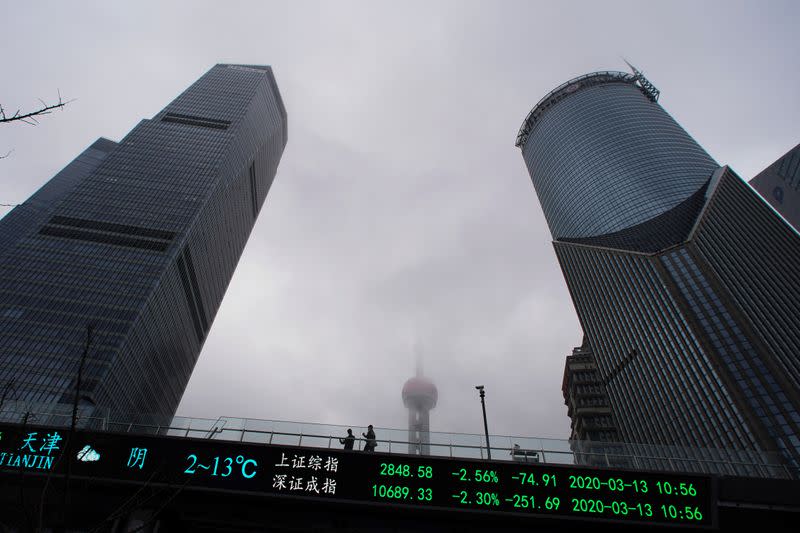 People are seen on a pedestrian overpass with an electronic board showing the Shanghai and Shenzhen stock indexes in Shanghai